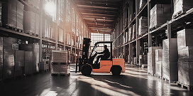 A worker uses a forklift to carry pallets with packages in a large warehouse