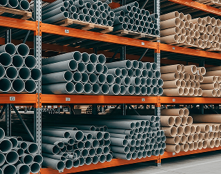 Various metal pipes sit in stacks on an orange shelving unit in a warehouse
