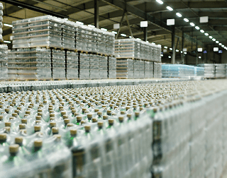 An image showing rows with several pallets of bottles wrapped in plastic in a warehouse