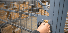 Hand locking a metal mesh warehouse cage door with stacked boxes visible inside.