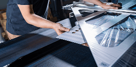 Worker operating a plastic wrapping machine to seal product packaging in a manufacturing facility.