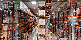 A worker uses a forklift to carry pallets with packages in a large warehouse