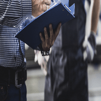 A worker holds a notepad and writes notes while another worker watches